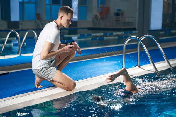 Genç adam oturmuş, yüzen bayan atleti seyrediyor.