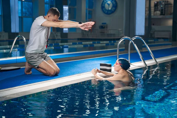 Kaukázusi edző a medence mellett, aki bemutatja a gyakorlatot a sportolónak. — Stock Fotó