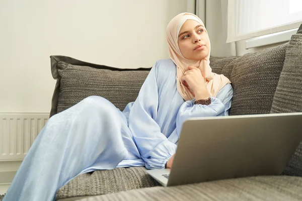 Mulher muçulmana sentada no sofá com laptop em casa — Fotografia de Stock