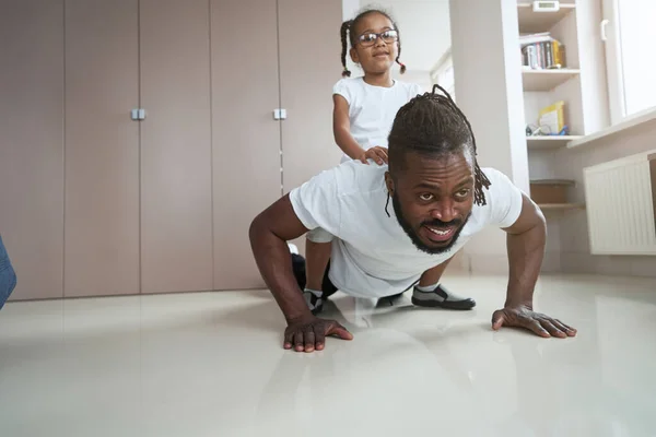 Erwachsener afroamerikanischer Vater macht Liegestütze mit seiner Tochter auf dem Rücken — Stockfoto