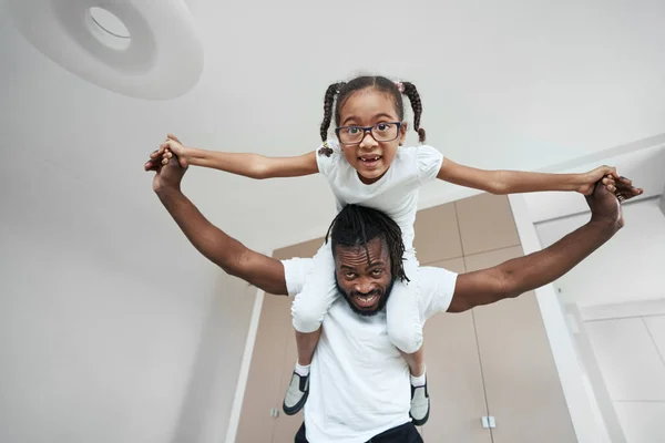 Afro ragazza americana si siede sul collo del padre con le braccia divaricate — Foto Stock