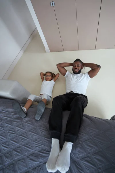 African American adult man is doing ab exercise with daughter — Stock Photo, Image