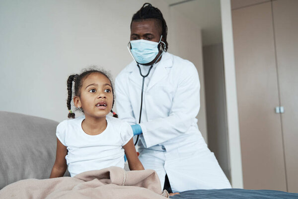 African American adult doctor listens to a girl with a stethoscope