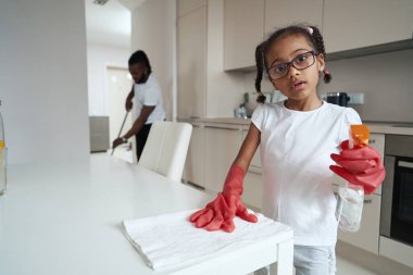 Küçük Afrikalı Amerikalı kız mutfakta babasının yanında mutfak masasını siliyor.