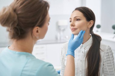Estetik terapist kozmetoloji kliniğinde kadının yüzünü kontrol ediyor.