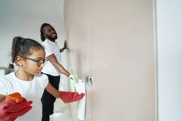 Adult african american man with daughter dusting on closet door — Stock Photo, Image