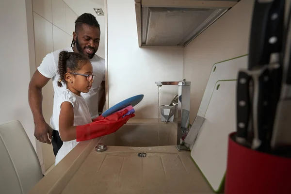 Uomo adulto guardando sua figlia lavare piatto nel lavandino — Foto Stock