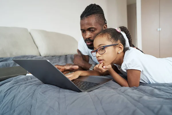 Adult father with daughter use gadget while lying in bed — Stockfoto