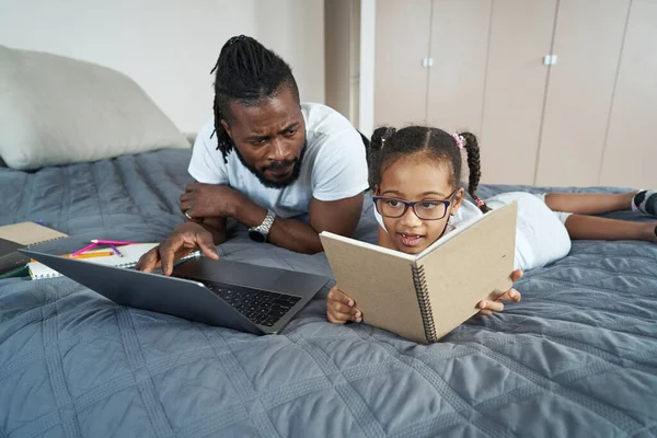 Adulto afro-americano padre con hija trabajo y estudio en cama — Foto de Stock