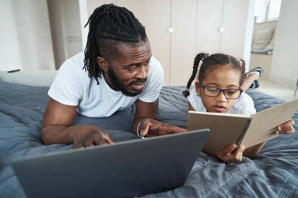Der erwachsene Vater mit seiner Tochter arbeitet und studiert im Bett — Stockfoto