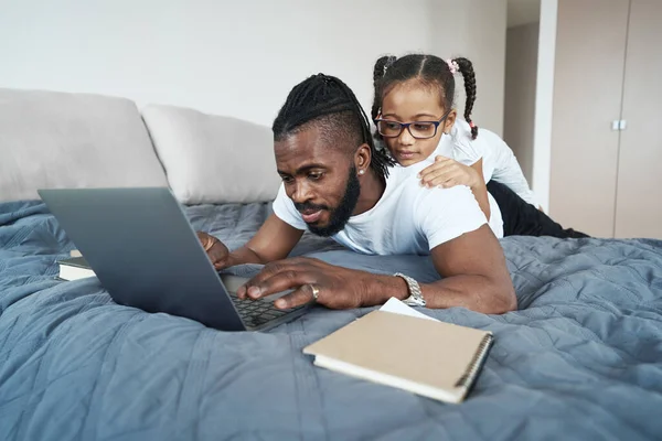 Little african american girl is lying on her working father — Fotografia de Stock