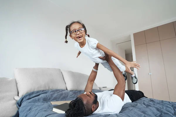 Hombre afroamericano adulto está levantando a su hija en la cama — Foto de Stock