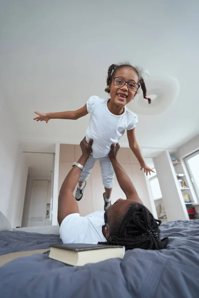 Erwachsener Afroamerikaner hält Tochter über sich im Bett — Stockfoto