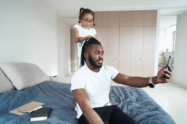 Ragazza afroamericana che gioca con i capelli di padre sul letto — Foto Stock