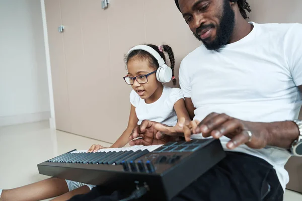 Hombre afroamericano tocando el sintetizador en el suelo junto a su hija — Foto de Stock