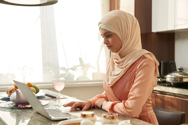 Müslüman kadın evde modern laptop kullanıyor.