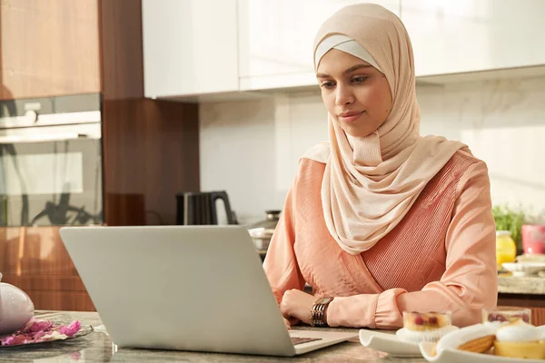 Evdeki mutfakta defter kullanan Müslüman kadın.