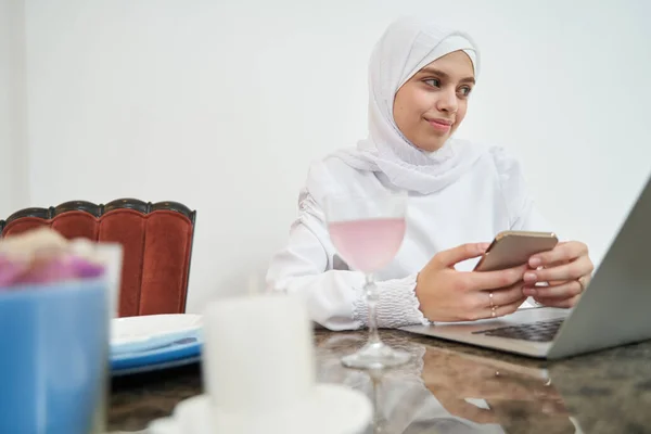 Mulher muçulmana usando smartphone e notebook em casa — Fotografia de Stock