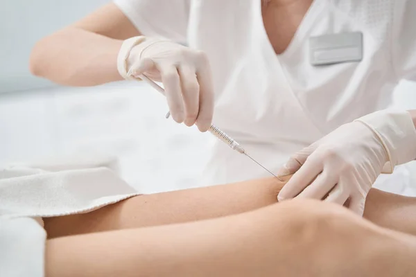 Woman receiving knee injection in cosmetology clinic — стоковое фото