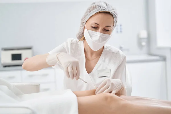 Cosmetology doctor doing injection into female knee — Stockfoto