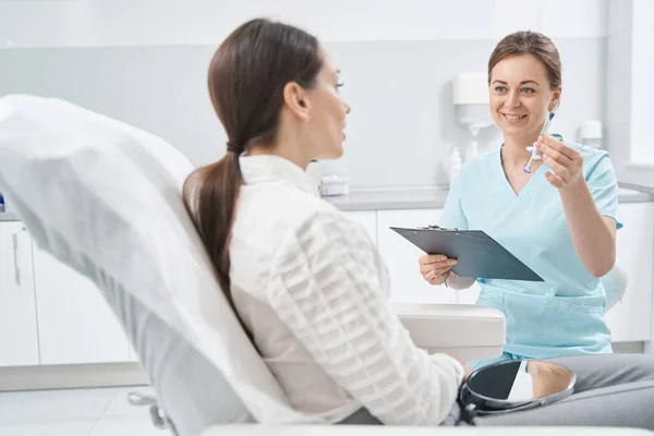 Médico alegre mostrando seringa para mulher no salão de beleza — Fotografia de Stock