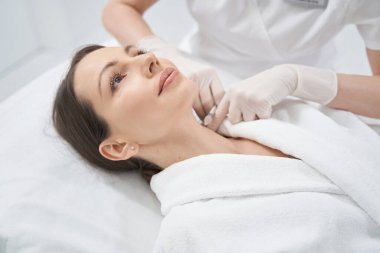 Doktor güzellik uzmanı klinikte kadının boynuna iğne yapıyor.