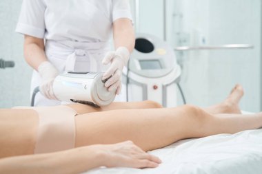 Kalça selülitini azaltıp deri dokusunu gençleştirirken sonosfer cihazını kullanan güzellik salonu çalışanı.