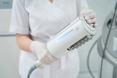 Cosmetologist in beauty shop holding body care device for cellulite removal and skin rejuvenation