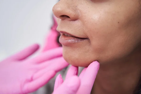 Zwei Hände in sterilen rosa Handschuhen berühren das weibliche Gesicht — Stockfoto