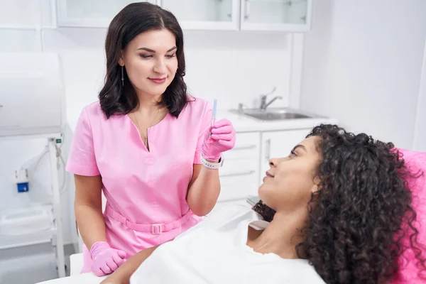 Arzt in Arztuniform zeigt Frau in der Nähe liegende Spritze — Stockfoto