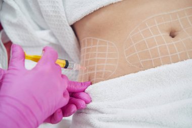 Pembe eldivenli kozmetolojistin yakın plan portresi estetik klinikteki deri altı yağına enjeksiyon yapıyor.