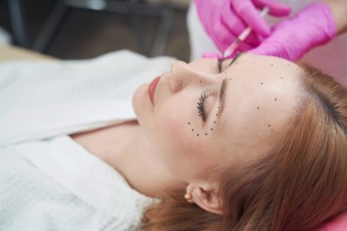 Güzel beyaz kadının yan görüş portresi kozmetik kürsüsünde uzanıyor ve güzellik kliniğinde yaşlanma karşıtı bir prosedür uygulanıyor.