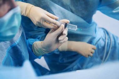 Cerrahi uzmanı ameliyat sırasında hemşireden şırınga ve ilaç alıyor.