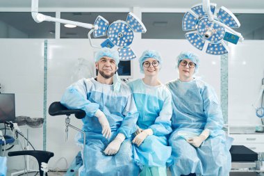 Tıp merkezindeki cerrahi yatakta otururken iki kadın asistanın poz verdiği bir cerrahi uzmanı.