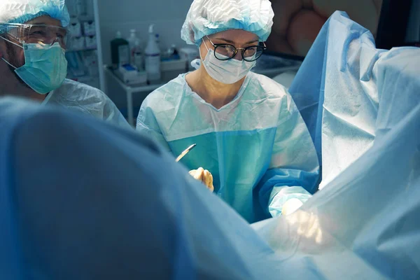 Cirurgiã Olhando Para Área Operada Enquanto Obtém Instrumento Laparoscópico Assistente — Fotografia de Stock