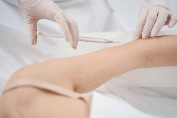 Close up of doctor cosmetologist with syringe making injection into female hand in beauty salon