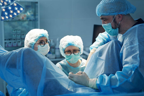 Male surgeon holding clamps while two female nurses performing operation in a pelvic area