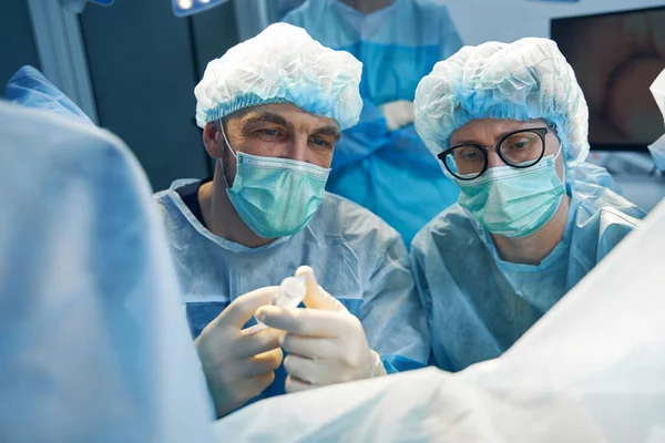외과의사 경험있는 간호사로서 주사기를 준비하면서 환자의 신체의 부위를 살펴보고 — 스톡 사진