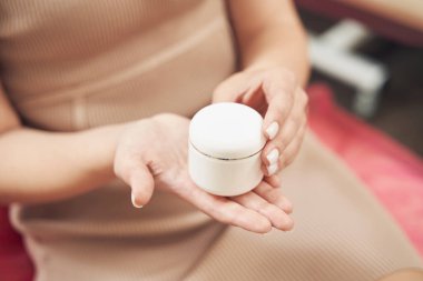 Kapalı bir odada elinde bir kavanoz nemlendirici krem tutan tanınmamış kişinin portresi.