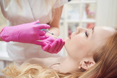 Güzellik salonunda çeneye yaşlanma karşıtı iğne yaptıran çekici genç bir kadının belden yukarısı portresi.