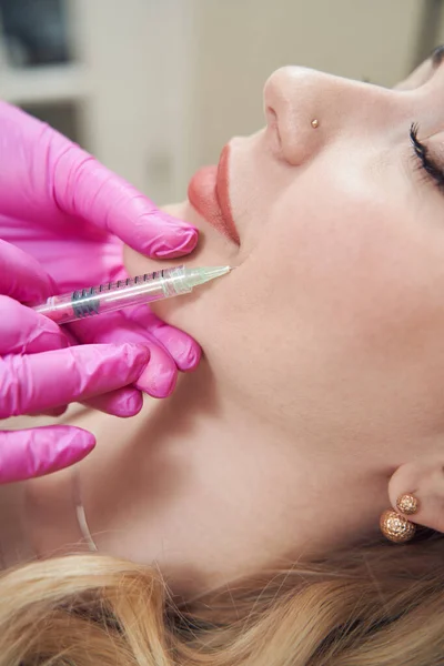 Cropped head side view portrait of elegant lady receiving anti aging injection into the chin in beauty salon