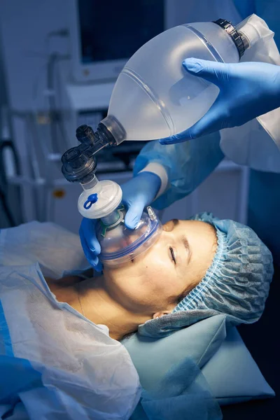Face of a woman on the operation table and a doctor giving her the mask inhalation anesthesia