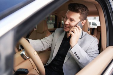 Erkek girişimci araba sürerken telefonla konuşuyor ve gülümsüyor.