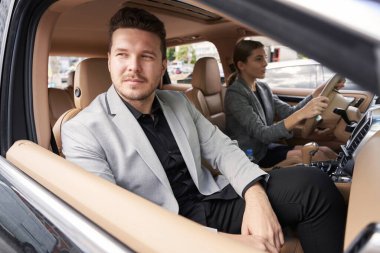 Araçta yolcu koltuğunda oturan sakallı beyefendi ve kadın otomobil kullanırken otomobil camından dışarı bakan adam.