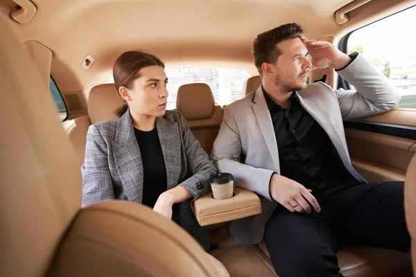 Serious lady and gentleman work colleagues sitting next to each other during business trip by car