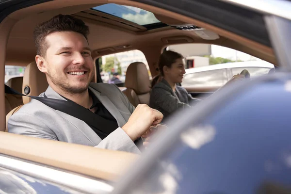 Smiling gentleman sitting on passenger seat in vehicle and holding bottle of water while lady driving automobile