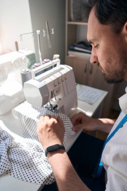 Masada oturan ve atölyede retro tarzı aşınma üretmek için dikiş makinesi kullanan bir adamın üst görünümü