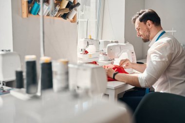 Genç adam masanda makara ile oturuyor ve modern ekipmanları kırmızı bez olarak kullanıyor.