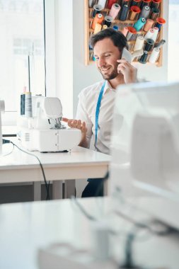 Gülümseyen terzi atölyede oturuyor ve ortaklarla istiridye yeme çağrısı yapıyor.