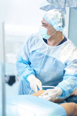 Tıbbi maske takan erkek doktor, ultrasonla bacağı incelerken video monitörüne bakıyor.